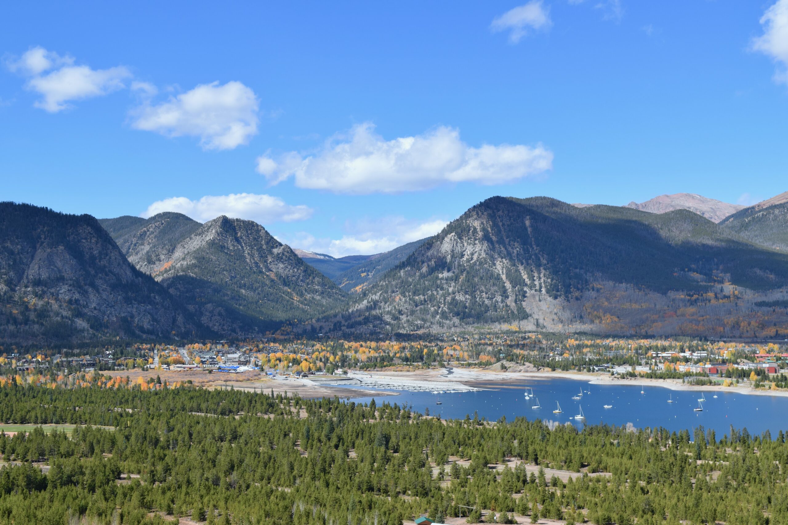 Landscape of Frisco Bay Marina in the early evening in autumn, featuring blue water, green pines, and golden aspen trees under a partly cloudy blue sky.
